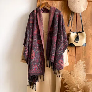 Detail van rode paisley kasjmier-achtige sjaal met zwarte franjes op beige jas