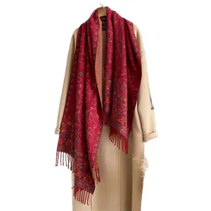 Ethnic floral red shawl with tassels styled over a beige wool coat on white background