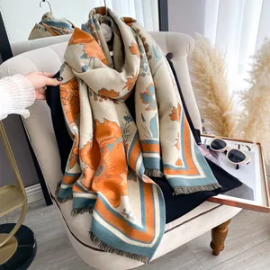 Detail of floral print cashmere-feel scarf with fringe hanging on a beige chair