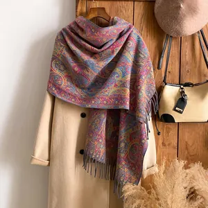 Détail d'un châle pashmina à motif paisley avec franges porté sur un manteau d'hiver beige