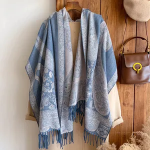Blue-grey and beige paisley jacquard pashmina scarf with fringe hanging on wooden wall