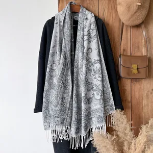 Detail view of ethnic paisley pattern scarf with thick white fringes on a dark wool coat
