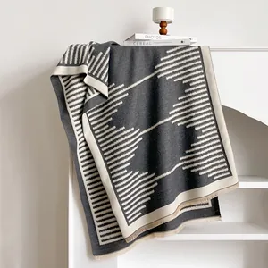 Modern cashmere-like shawl with gray geometric patterns and tassel details on a white shelf