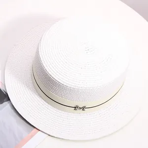 Close-up of white woven straw boater hat with beige ribbon and silver M metal buckle