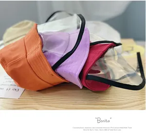 Close-up of colorful cotton bucket hats with clear PVC protective face shields on wood