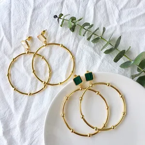 Detail of gold geometric hoop earrings with malachite and mother of pearl square studs