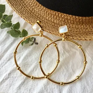 Detailed view of large gold hoop earrings with white shell inlay on a natural background