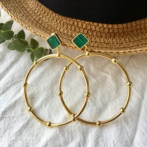 Close-up of gold hoop earrings with green malachite inlay on white textured background