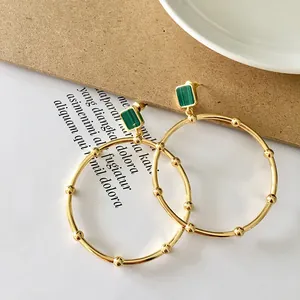 Detailed view of large gold hoop earrings with green malachite stones and bead accents