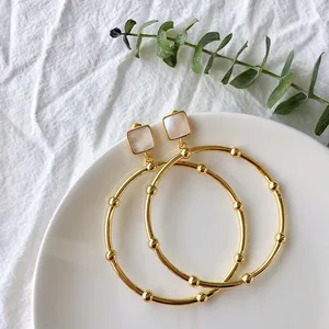 Detailed view of gold hoop earrings featuring square shell studs and beaded accents