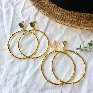 Golden round hoop earrings with malachite and pearl accents on white fabric background