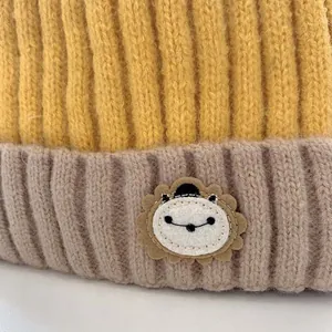 Detailaufnahme der gelb-braunen Rippstrickmütze mit einem süßen Löwen-Aufnäher für Babys