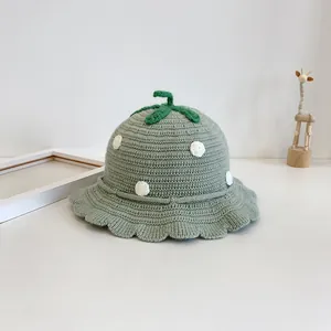 Close-up of knit baby hat with green ruffle brim, white polka dots and leaf stem detail