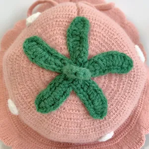 Detail of pink knitted strawberry hat for babies showing green leaves and white dots