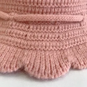 Close-up of pink knitted baby hat featuring thick stitch texture and scalloped wavy edges