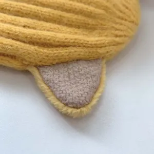 Makrodetail einer ingwergelben Strickmütze für Babys mit 3D-Tierohr-Applikationen