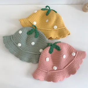 Detailed view of handmade strawberry knit hats in yellow, green, and pink for babies