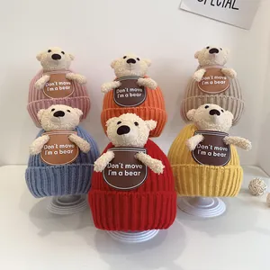 Detailed view of knitted baby beanies in six colors featuring plush bear decorations