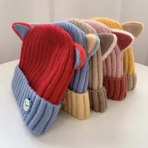 Detail von bunten Strickmützen mit Katzenohren, dicker Rippstruktur und Bären-Aufnäher