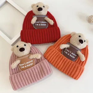 Detail of knitted baby beanies with 3D plush bear and embroidered quote patch
