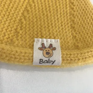 Close-up of yellow knit baby hat featuring deer pattern label and soft yarn texture