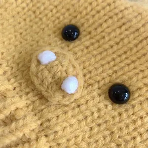 Close-up of yellow knit baby hat with decorative black buttons and cute cartoon features