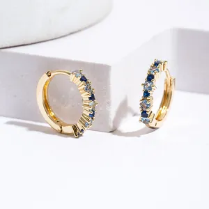 Golden huggie hoops with blue and clear zircon inlay on white geometric stone props