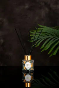 Detailed close-up of a glass reed diffuser with golden cap and black aroma sticks