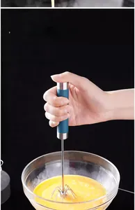 Manual stainless steel whisk mixing egg yolks in a glass bowl with blue ergonomic handle