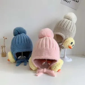 Nahaufnahme von Strickmützen mit Ohrenklappen, Pompons und gelben Enten-Applikationen