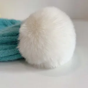 Nahaufnahme einer weißen Kunstfell-Bommel an einer blaugrünen Baby-Strickmütze für den Winter
