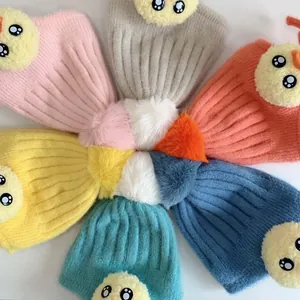 Flach liegende bunte Strickmützen für Kleinkinder mit Bommeln und Kükenmotiven