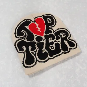 Detail of Y2K beige knit beanie with black TOP TIER text and a red broken heart pattern