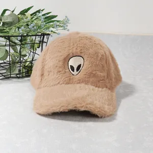 Detailed texture of khaki plush baseball cap with alien head embroidery on gray surface