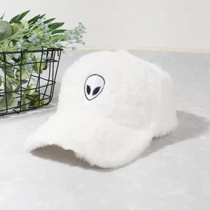 Close-up of white plush baseball cap with black alien embroidery and soft texture