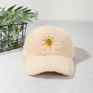 Détail d'une casquette en peluche beige avec broderie soleil jaune sur texture douce en velours