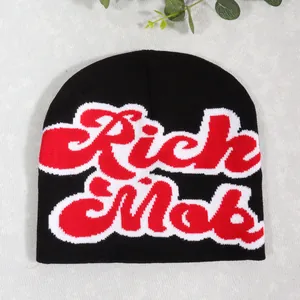 Detail of a black knitted beanie featuring red and white Rich Mob jacquard lettering
