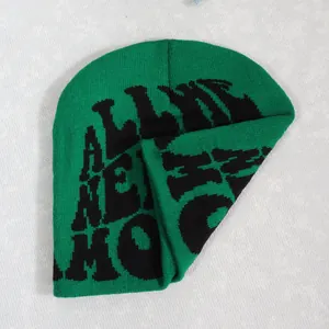 Detailed view of green ribbed knit beanie featuring black letter patterns on a grey background
