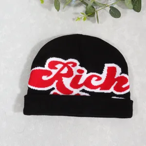 Close-up of black knitted beanie featuring red Rich embroidery with white outline detail
