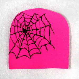 Detail of bright pink knitted beanie featuring a black spider web pattern on a white fabric