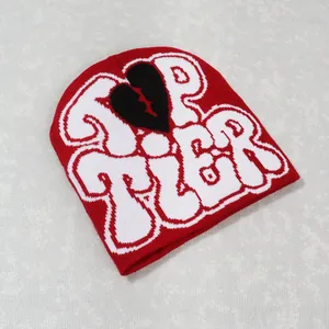 Detail of red knit beanie featuring white Top Tier text and black broken heart pattern