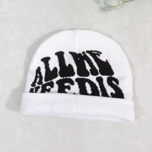 Detailed close-up of a white knit beanie featuring black jacquard letter embroidery