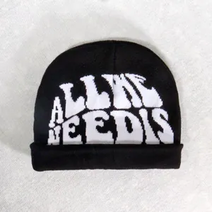 Close-up of black knitted beanie featuring white ALL I NEEDS jacquard text and folded cuff