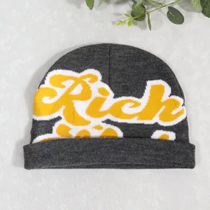 Close-up of dark grey knitted beanie featuring yellow Rich lettering in jacquard weave