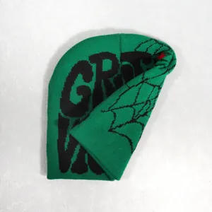 Detailed close-up of green knitted beanie with black spider web and letter jacquard texture