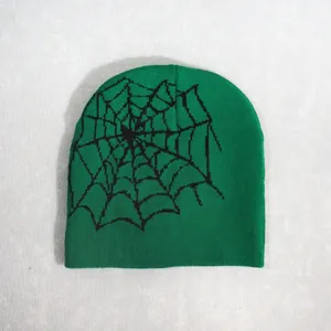 Detail view of a green knitted beanie featuring a black spider web pattern for winter warmth