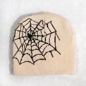 Close-up of beige knit beanie featuring a black spider web pattern for streetwear style