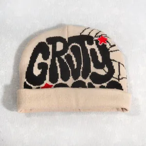 Detail of beige knitted beanie featuring black graffiti text and red star embroidery