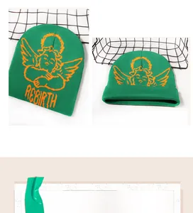 Detail of green knit beanie with orange angel wings and REBIRTH lettering texture