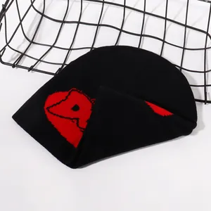 Detail of black knit beanie featuring bold red geometric jacquard pattern on street style